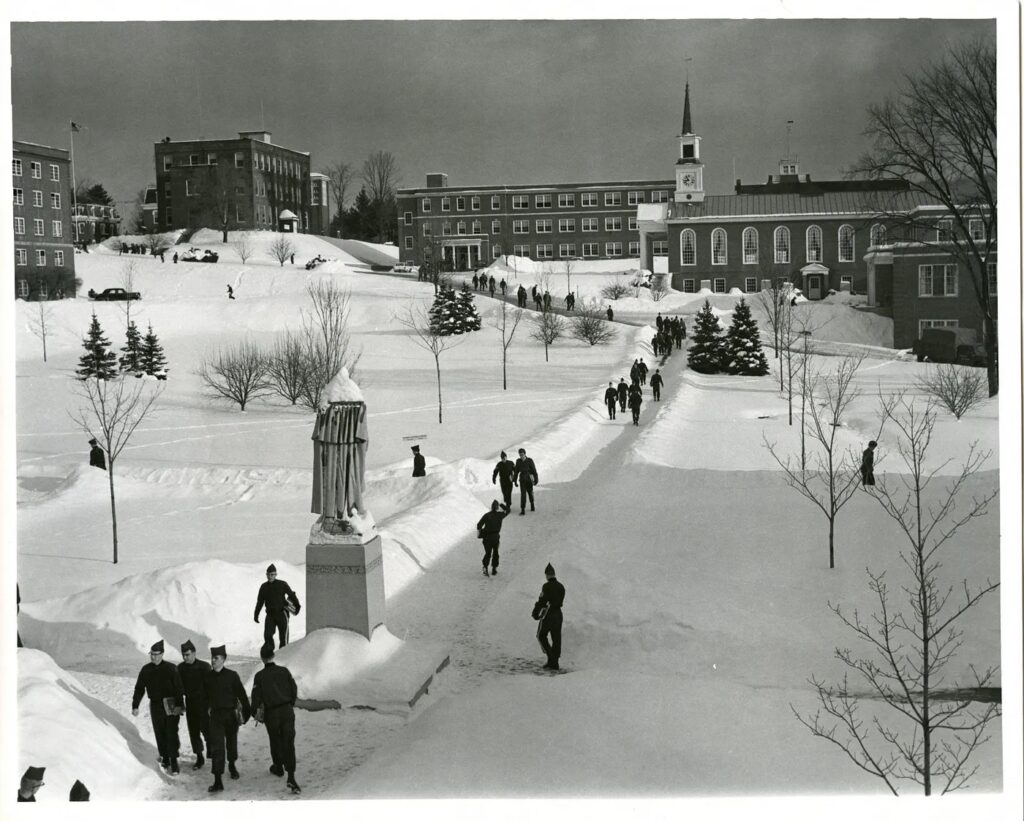 Photograph of Norwich University circa 1969 with snow covered quad.  Red brick academic buildings and barracks.  Cadet Chapel.  Part of biography of Dr. Anthony J. Carbone.