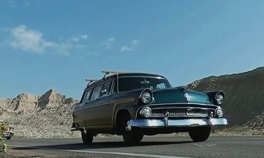 Photograph of an old woody station wagon driving along Fort Irwin Road through the Mojave Desert.  Biography of Dr. Anthony J. Carbone