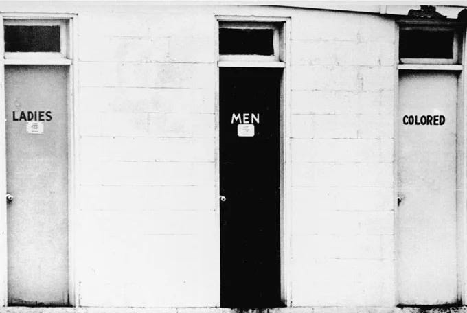 Photograph of doors to three rest rooms, one “Ladies”, one “Men”, and one labeled “Colored” from the Deep South. BIography of Dr. Anthony J. Carbone.