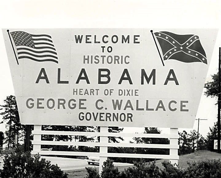 Photograph of an Alabama welcome sign that says "Welcome to Historic Alabama, Heart of Dixie, George C. Wallace, Governor. Biography of Dr. Anthony J. Carbone.